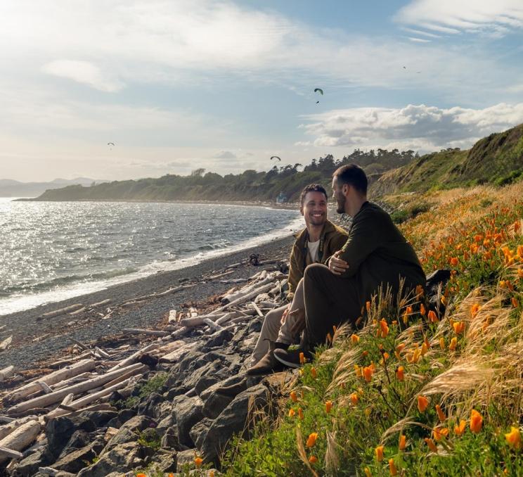 A couple sits oceanside along Dallas Road beach in Victoria, BC