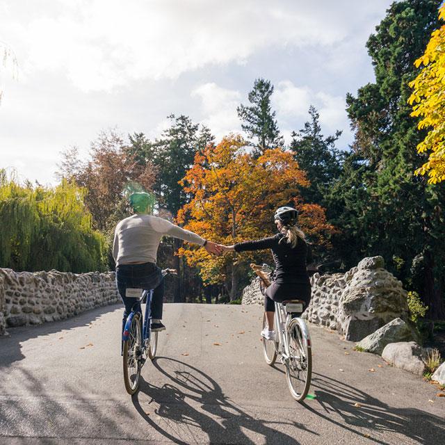 A couple holds hands as the cycle through Beacon Hill Park in Victoria, BC.