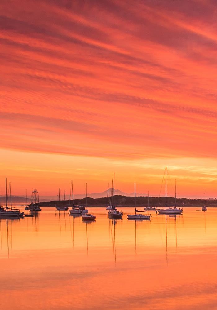 Boats sit on the water during a fiery red sunrise at the Oak Bay Marina in Victoria, BC