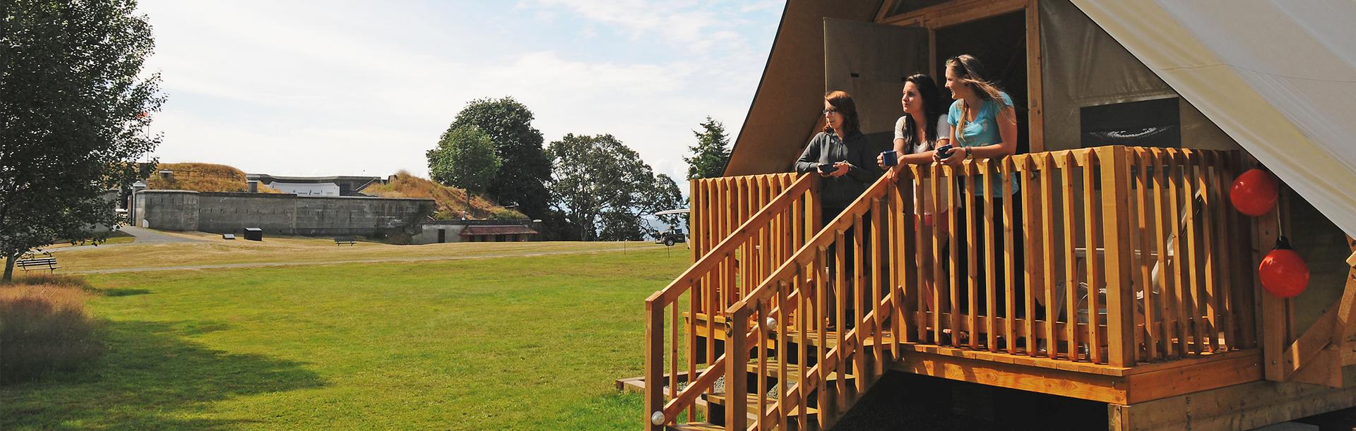 A group of friends stand on the porch of an oTENTiks tent at Fort Rodd Hill & Fisgard Lighthouse National Historic Site in Victoria, BC