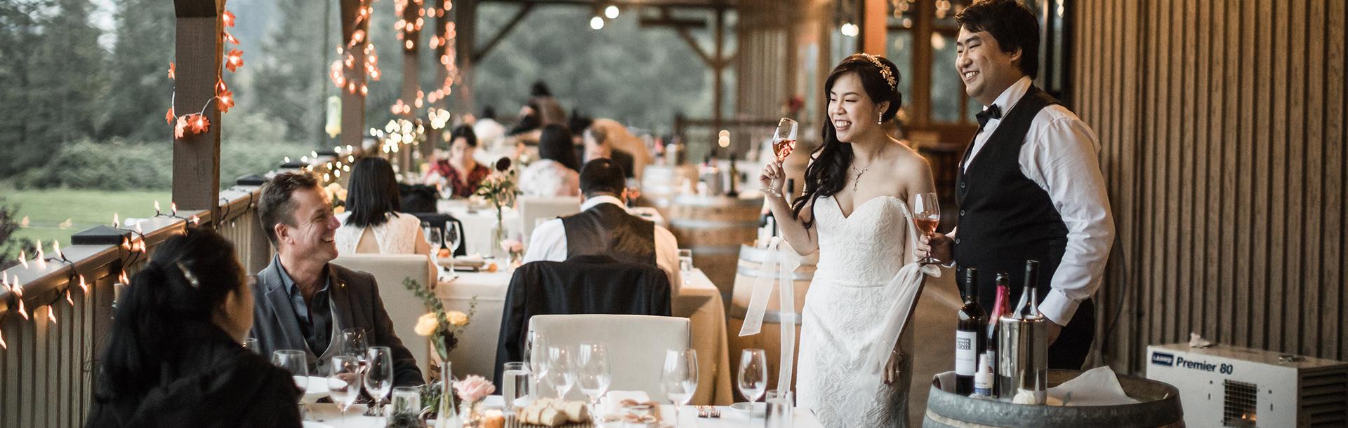 A bride and groom mingle with guests, champagne in-hand, on the patio at Church & State Wines during a wedding in Victoria, BC