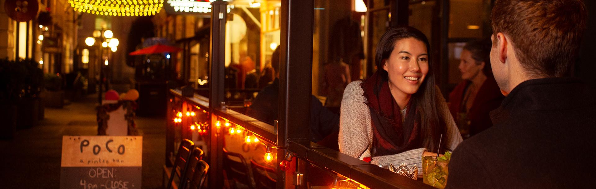 A young couple dines on a patio in Trounce Alley at night in Victoria, BC
