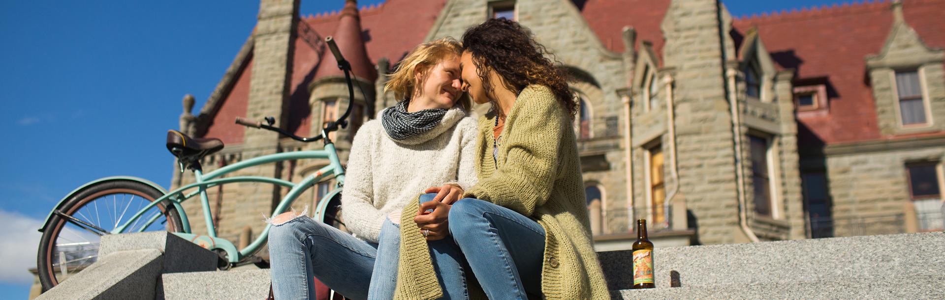 A couple sits on the steps of Victoria Castle in front of a blue bike in Victoria, BC