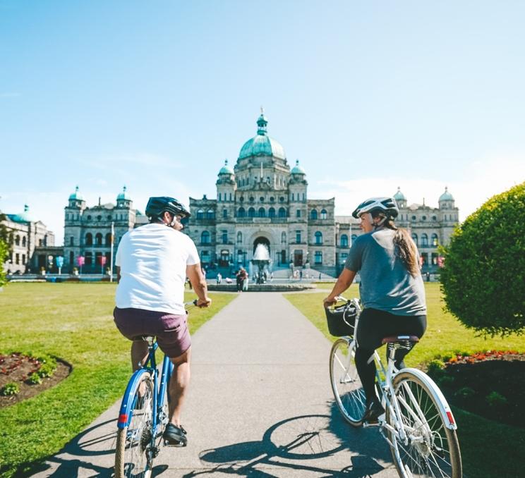 A pair of cyclists ride their bikes towards the BC Parliament Buildings in Victoria, BC