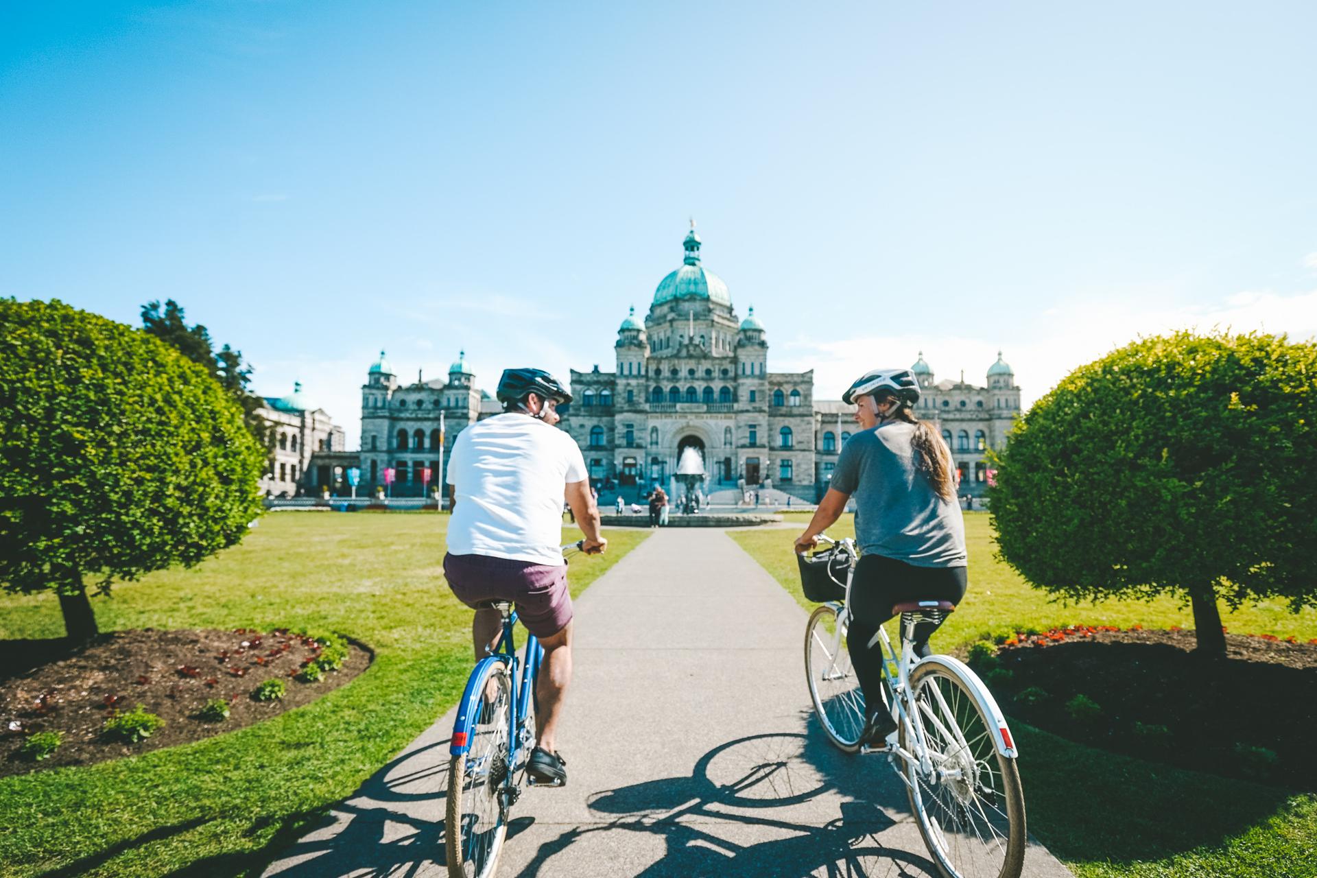 A pair of cyclists ride their bikes towards the BC Parliament Buildings in Victoria, BC