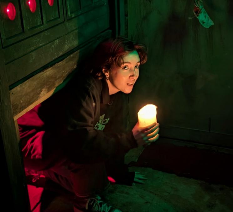 A woman crawls through an exit with a candle at Horror Escape Victoria in Victoria, BC