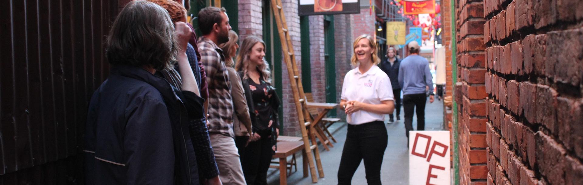A woman in a white shirt leads a food tour down Fan Tan Alley, the narrowest street in Canada, during a walking food tour in Victoria, BC