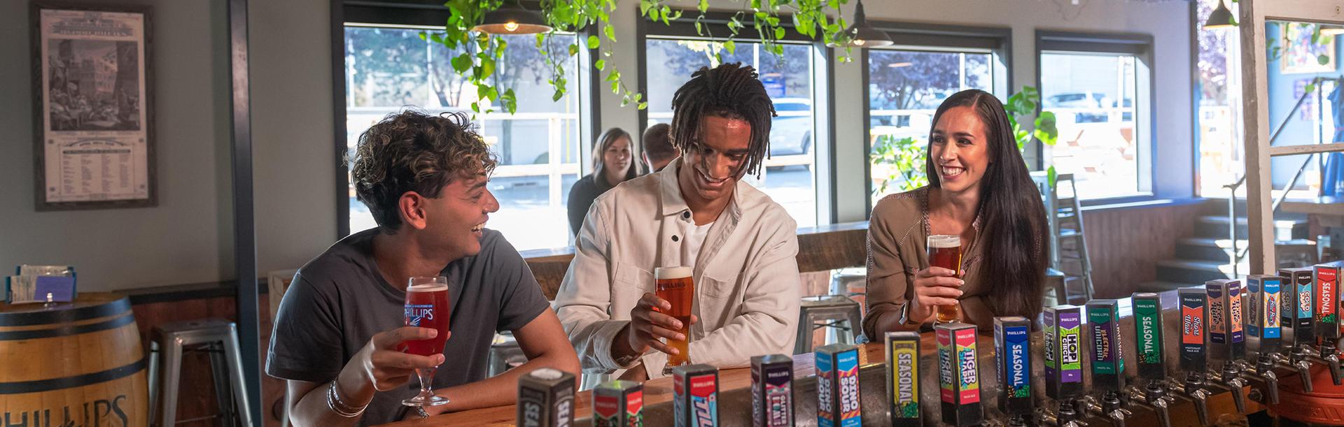 Three friends enjoy beers at the bar in the taproom of Phillip's Brewing Co. in Victoria, BC