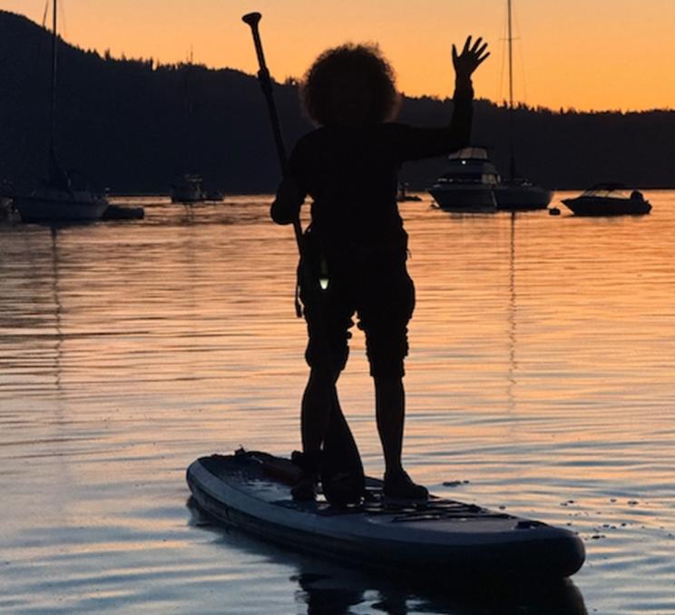 A paddleboarder waves at the camera during a sunset paddelboarding tour with South Island SUP in Victoria, BC