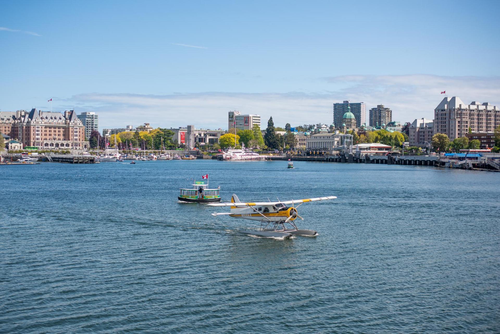 A Kenmore Air seaplane flight taxis across Victoria's Innner Harbour, while a Victoria Harbour Ferry passes in the background, in Victoria, BC