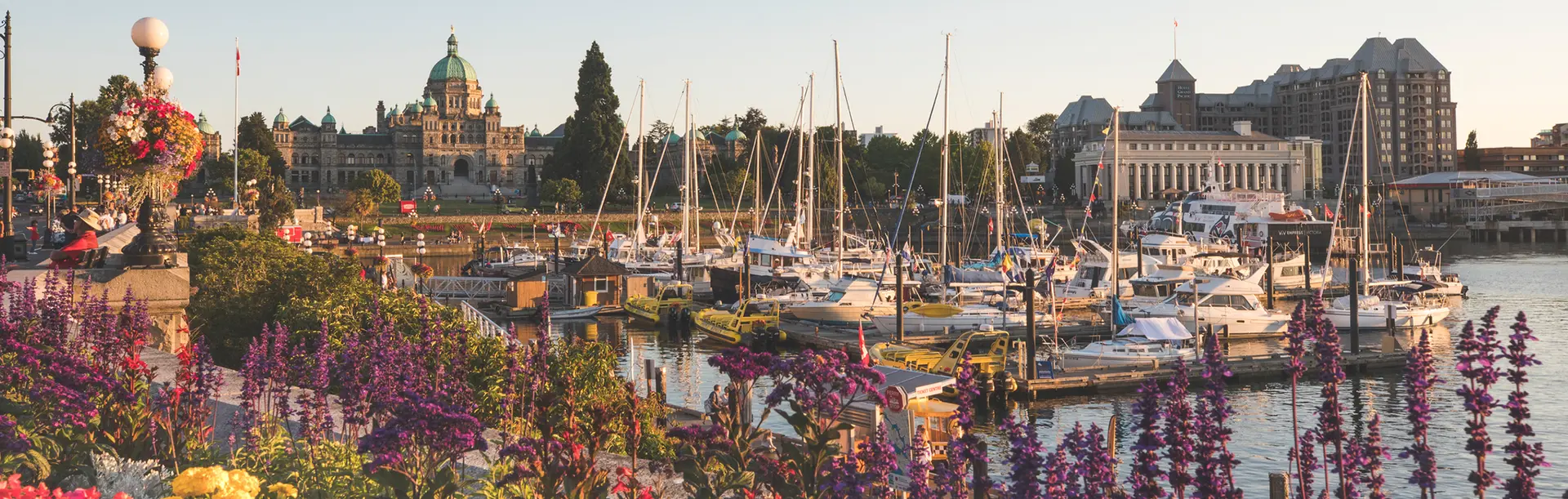 Springtime along Victoria's Inner Harbour with flowers in the foreground as boats fill the harbour, all backdropped by the BC Parliament Buildings in Victoria, BC
